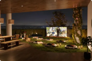 Outdoor night lounge under a wooden ceiling with a fire pit and floor cushions; a projector screen shows a movie in a landscaped garden.