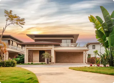 Modern two-story house with brick and wood exterior, a wide driveway, and tropical plants in the front yard.