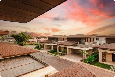 Sunset casts warm orange-pink light over a quiet suburban street lined with modern houses and green trees.