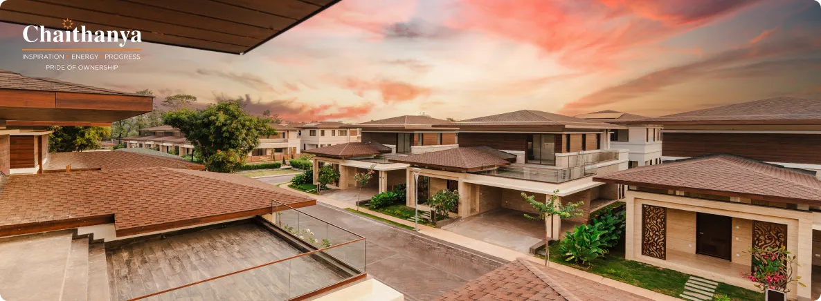 Aerial view of a modern villa-style complex with brown tiled roofs, glass railings, and lush landscaping at sunset; Chaithanya branding in the corner.