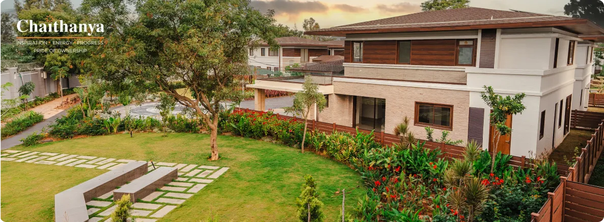 Modern two-story house with a landscaped front yard, stone stepping paths, and vibrant greenery, featuring Chaithanya branding in the upper-left corner.