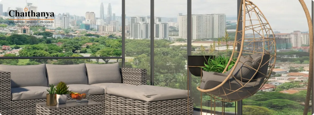 Modern balcony lounge with grey cushioned wicker sofa, a hanging egg chair, and potted plants, overlooking a city skyline; Chaithanya logo in corner.