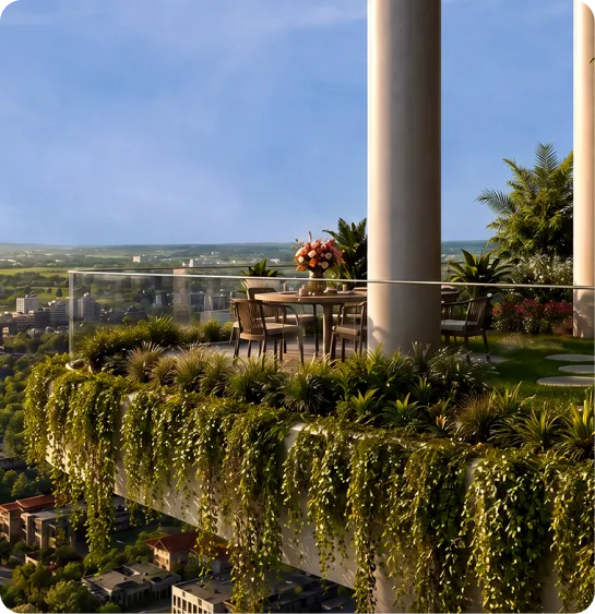 Outdoor rooftop terrace with a round table and chairs, potted flowers, and trailing greenery along a glass railing overlooking a distant cityscape.